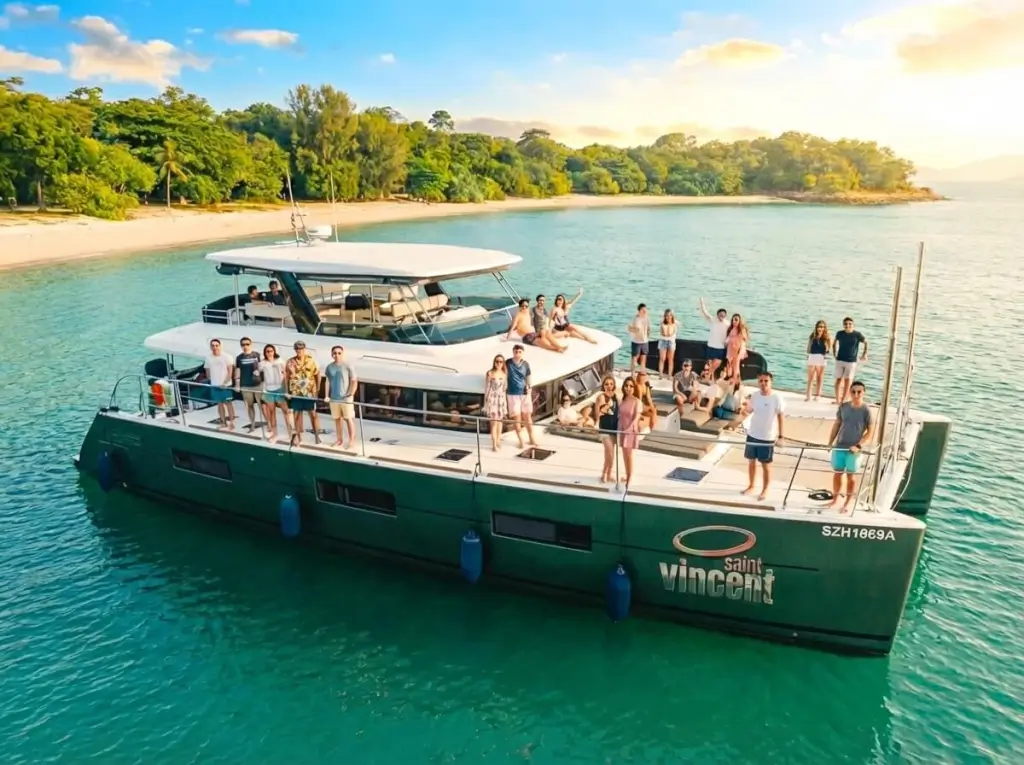 Lagoon 630: St. Vincent Yacht Singapore - A large group of people are posing and relaxing on a dark green catamaran named 'Saint Vincent' in clear turquoise water at ONEΒ°15 Marina Club, Singapore