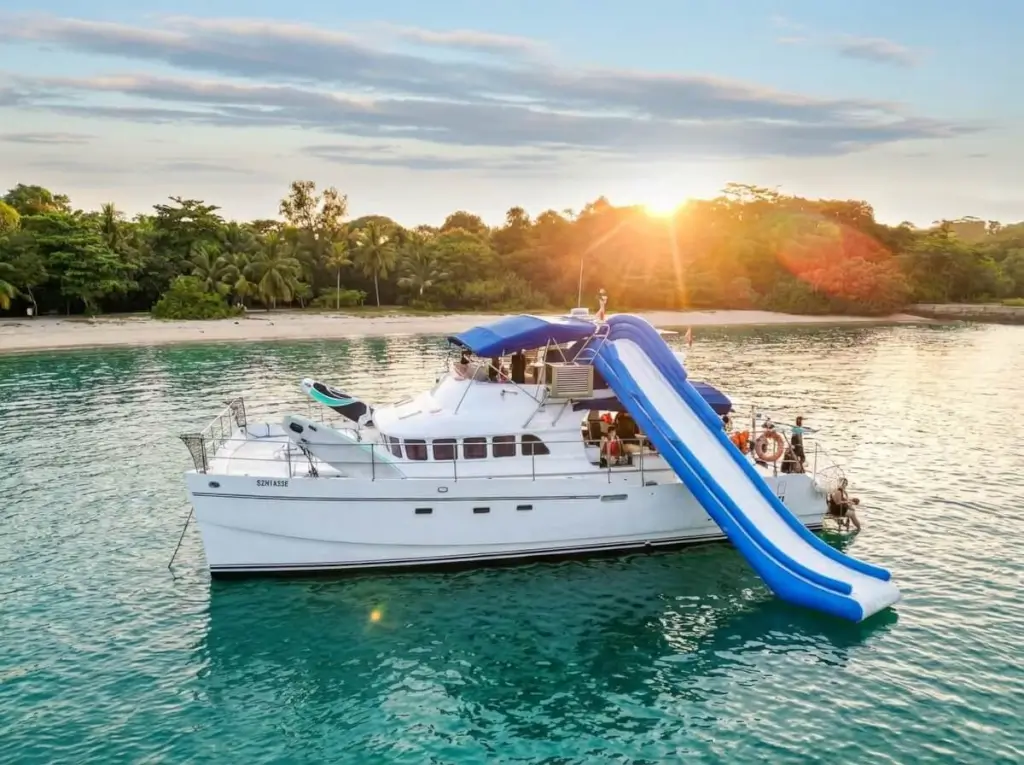 Power Catamaran - Kingdom Yacht Singapore - A large white catamaran with a blue inflatable slide extending into calm turquoise water at Marina at Keppel Bay, Singapore